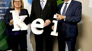 Drei Personen halten gemeinsam die drei Buchstaben des KEIs vor die Kamera