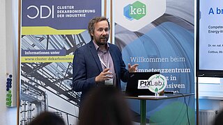 Dr. Kai Winkelmann, Fachgebietsleiter Think Tank und cluster Dekarbonisierung der Industrie steht vor einem Rollup des KEI und des CDI und hält einen Vortrag anlässlich des Besuchs der indischen Delegation.