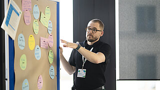 Ein Mann präsentiert Ergebnisse beim Workshop auf einer Korktafel mit bunten Zetteln