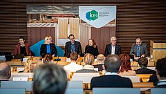 Sechs Personen sitzen vor einem gefüllten Hörsaal am Podium.
