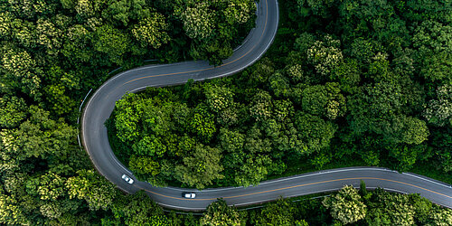 Eine geschwungene Autostraße aus der Vogelperspektive umgeben von grünem Wald 