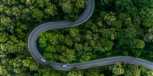 Eine geschwungene Autostraße aus der Vogelperspektive umgeben von Wald 