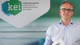 ein Mann steht vor einem farbigen Hintergrund mit Logo des KEIs