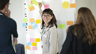 lächelnde Frau beim Workshop vor einer Tafel mit bunten Zetteln