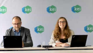 zwei Personen sitzen vor Laptops, an der Wand im Hintergrund ist mehrfach das Logo des KEIs abgebildet