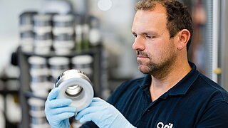 Ein männlicher Mitarbeiter der QSIL Ceramics GMBH betrachtet ein Bauteil aus Keramik.