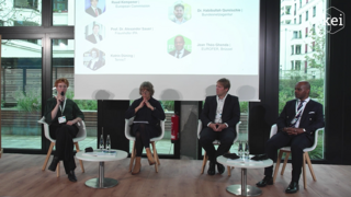 mehrere Personen sitzen auf Stühlen vor einer Glaswand bzw einem sehr hohen Fenster