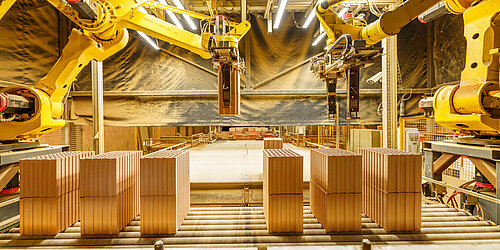 Fabrikszene mit zwei Roboterarmen die Ziegelsteine auf das Förderband legen