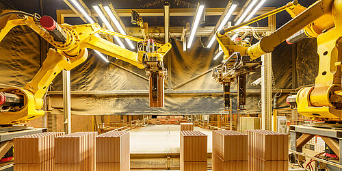Fabrikszene mit zwei Roboterarmen die Ziegelsteine auf das Förderband legen