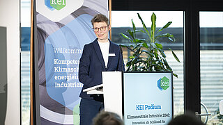 Frau mit Brille vor KEI Roll Up und Podium