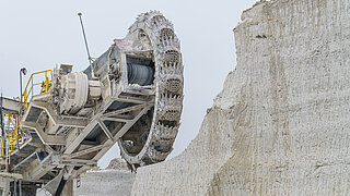 Bagger gräbt sich in Gesteinswand und baut Gestein für die Zementherstellung ab.