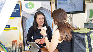 Monica Villanueva spricht mit einer Besucherin am Informationsstand des KEI