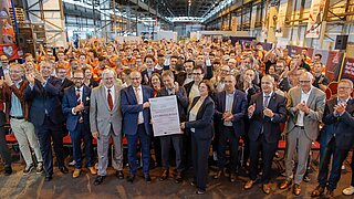 Gruppenbild mit Bundesminister Habeck, dem Management und der Belegschaft von ArcelorMittal Eisenhüttenstadt bei der Fördermittelbescheidübergabe im Stahlwerk.