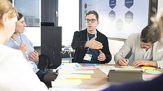 Gruppenarbeit im Workshop: die Teilnehmenden sitzen um einen Tisch und notieren ihre Gedanken auf bunten Merkzetteln. 