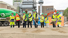Die Geschäftsführer und Ehrengäste vollziehen beim Baustart des Projektes "Cap2U" den ersten spatenstich. Mit Helmen und Warnwesten ausgekleidet graben sie mit Spaten Sand aus.